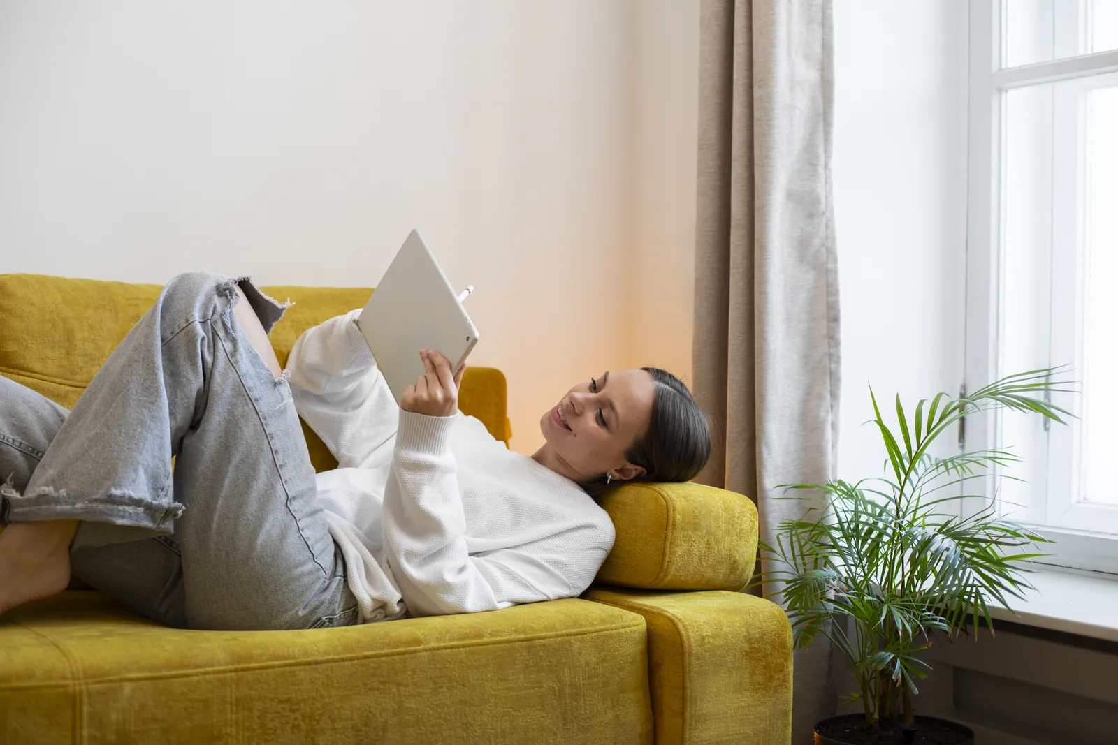A woman relaxing on a sofa, reading on a tablet in soft natural light
